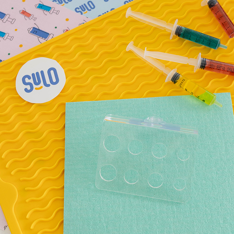 Colorful syringes with The Syringe Caddy on a branded Sulo background.