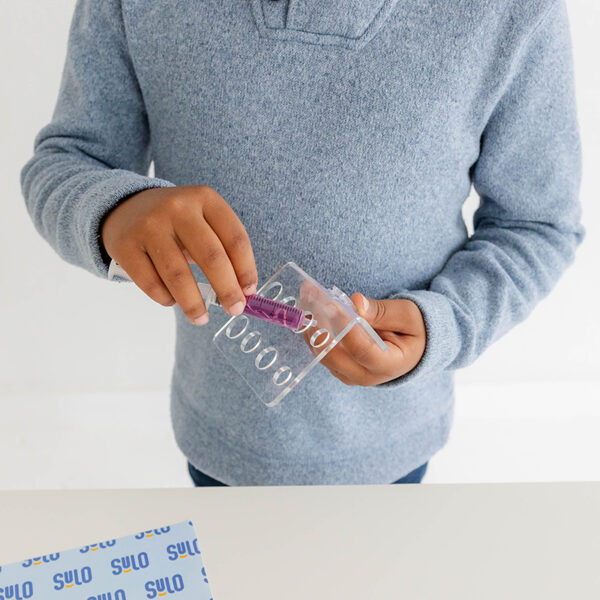 Child inserting a medicine storage for syringe into The Syringe Caddy tray.