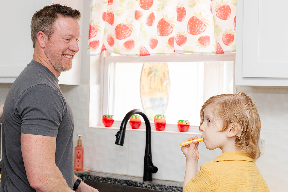 Dad smiling at child using an oral syringe created by a family-owned business
