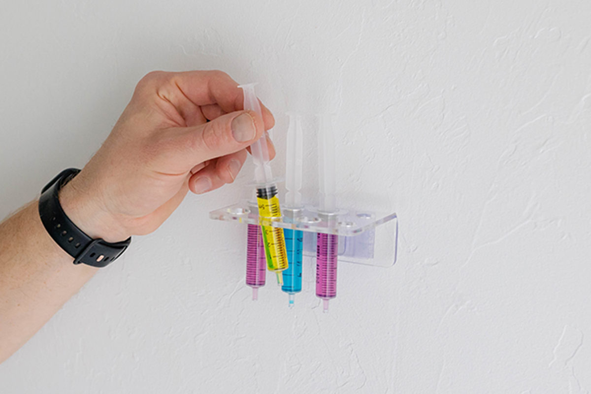 Hand placing a syringe into wall-mounted Syringe Caddy to Prevent Cross Contamination