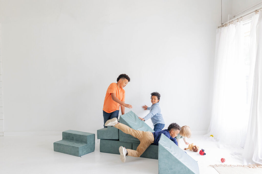 Three young children laughing and playing with cushions on the floor as a healthy family.